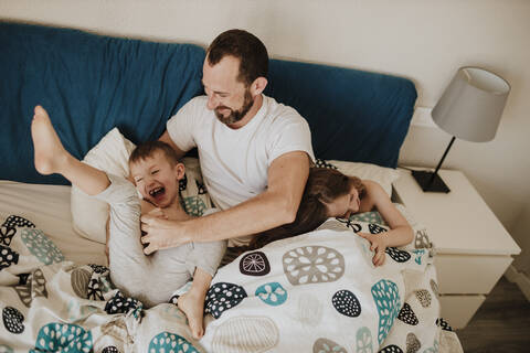 Vater spielt mit fröhlichen Kindern auf dem Bett zu Hause, lizenzfreies Stockfoto