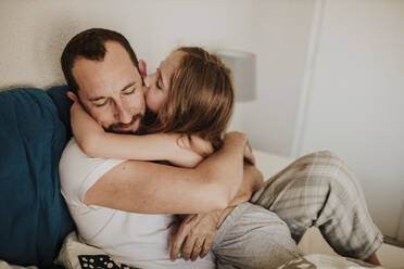 Tochter küsst Vater auf die Wange beim Umarmen auf dem Bett zu Hause - GMLF01008