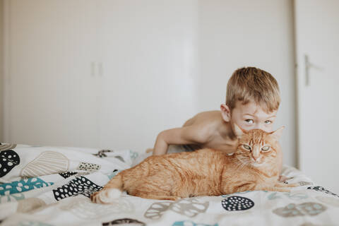 Boy kissing ginger cat on bed at home stock photo
