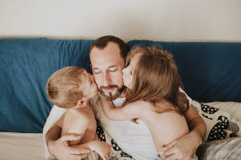 Daughter and son kissing father on cheek in bedroom at home stock photo