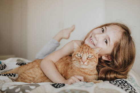 Cute smiling girl with ginger cat on bed at home - GMLF01013