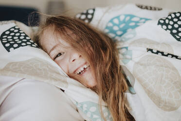 Lächelndes Mädchen in Decke eingewickelt auf dem Bett zu Hause - GMLF01015