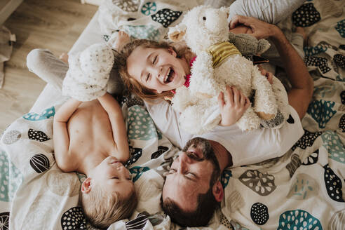 Lachender Vater und spielende Tochter, während sie mit ihrem Sohn zu Hause auf dem Bett liegen - GMLF01023
