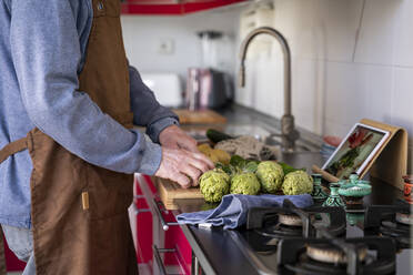 Senior man cutting vegetable during video call at kitchen counter - AFVF08237