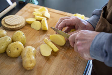 Älterer Mann schneidet rohe Kartoffeln auf einem Schneidebrett in der Küche - AFVF08245