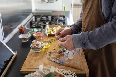 Älterer Mann mit Schürze schält Knoblauch auf einem Schneidebrett - AFVF08247