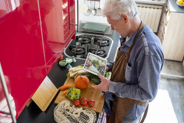 Senior man preparing food during video call with daughter while standing at kitchen counter at home - AFVF08254