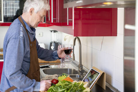 Senior man holding wine glass during video call at kitchen counter in home stock photo