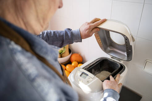 Senior man preparing bread in appliance at home - AFVF08258