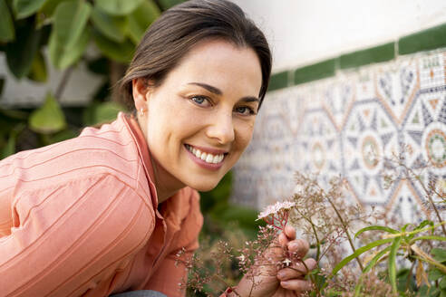 Schöne lächelnde Frau mit blauen Augen hält Blumen im Garten - AFVF08265