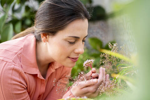 Junge Frau riecht an frischen Blumen im Garten, lizenzfreies Stockfoto