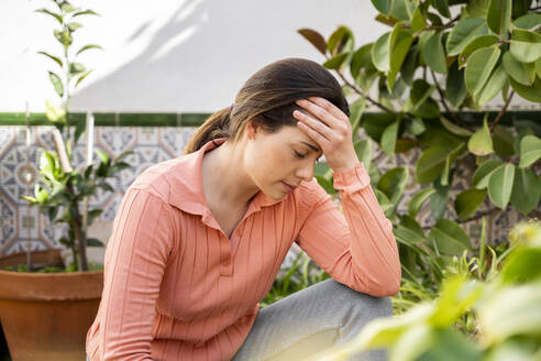 Tensed young woman with head in hand sitting in garden - AFVF08267