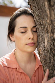 Schöne Frau mit geschlossenen Augen umarmt Baum im Garten - AFVF08270