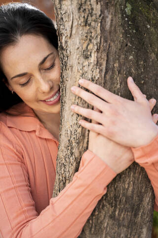 Affectionate woman embracing tree trunk in garden stock photo