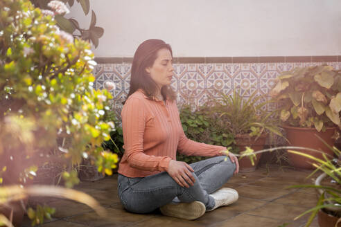 Junge Frau meditiert auf dem Boden sitzend auf einer Terrasse im Garten - AFVF08277
