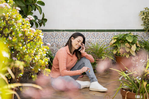 Lächelnde Frau, die im Garten sitzend mit ihrem Handy telefoniert - AFVF08279