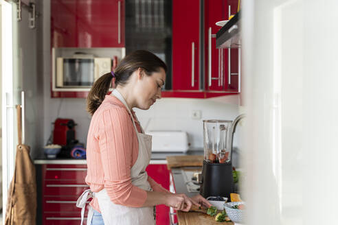 Young woman cutting strawberry in kitchen at home - AFVF08282