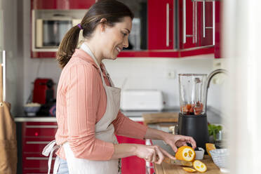 Schöne Frau schneidet Orangen auf einem Brett in der Küche zu Hause - AFVF08285