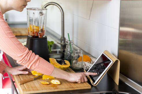 Young woman using digital tablet while preparing fruit smoothie in kitchen - AFVF08288