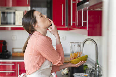 Schöne Frau leckt Finger bei der Vorbereitung Obst Smoothie in der Küche zu Hause - AFVF08290