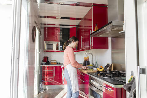 Young woman preparing food while standing in kitchen at home stock photo