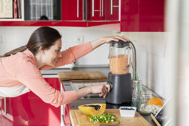 Woman using blender to prepare smoothie in kitchen at home - AFVF08296