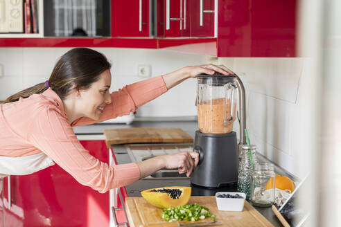 Frau verwendet Mixer zur Zubereitung eines Smoothies in der Küche zu Hause - AFVF08296