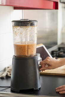 Young woman making smoothie through blender in kitchen at home - AFVF08297