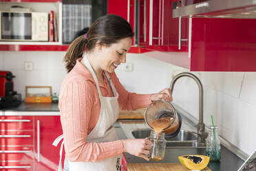 Schöne Frau gießt Smoothie in Einmachgläser in der Küche zu Hause - AFVF08298