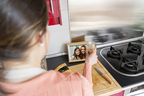 Junge Frau zeigt ihren Freunden per Videoanruf aus der Küche einen Smoothie, lizenzfreies Stockfoto