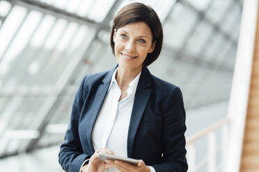 Smiling businesswoman with digital tablet in corridor - JOSEF03617