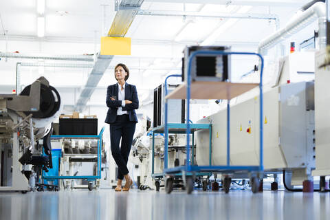 Female entrepreneur with arms crossed standing in factory stock photo