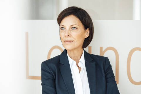 Confident businesswoman looking away in office against wall stock photo