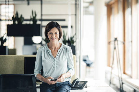 Glückliche Geschäftsfrau mit Smartphone im Büro, lizenzfreies Stockfoto