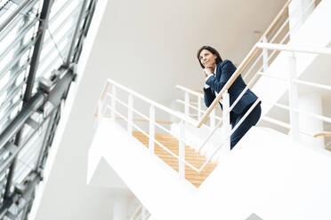 Thoughtful businesswoman with hand on chin leaning over railing in corridor - JOSEF03628