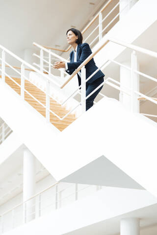 Businesswoman leaning on railing while standing over steps in corridor stock photo