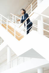 Businesswoman leaning on railing while standing over steps in corridor - JOSEF03632