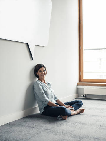 Smiling female entrepreneur sitting on floor in office against wall stock photo