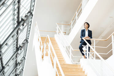 Female professional by railing standing on staircase in corridor - JOSEF03638