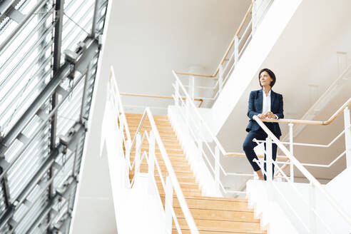 Weibliche Fachkraft am Geländer stehend auf einer Treppe im Korridor - JOSEF03638