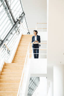 Mature businesswoman with digital tablet standing on steps at office - JOSEF03639