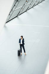 Geschäftsfrau mit Koffer, die im Flur steht und mit ihrem Smartphone spricht - JOSEF03646