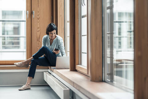 Businesswoman working on laptop while sitting by window at office stock photo