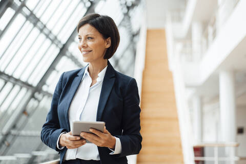 Selbstbewusste Geschäftsfrau mit digitalem Tablet, die im Korridor wegschaut, lizenzfreies Stockfoto