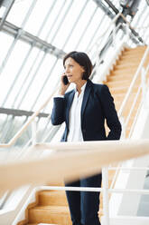 Female entrepreneur talking on smart phone while standing on staircase - JOSEF03657