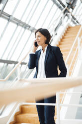 Unternehmerin, die auf einer Treppe stehend mit ihrem Smartphone telefoniert - JOSEF03657