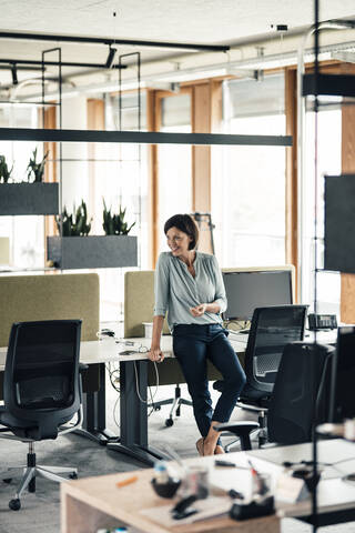 Unternehmerin lehnt sich im Büro an den Schreibtisch, lizenzfreies Stockfoto