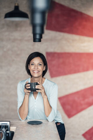 Lächelnde Geschäftsfrau mit Kaffeetasse im Büro, lizenzfreies Stockfoto