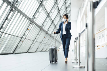 Female professional talking on smart phone while walking in corridor during pandemic - JOSEF03674