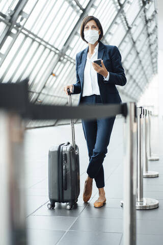 Businesswoman looking away with smart phone in corridor during COVID-19 stock photo